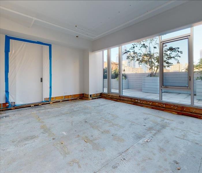 A room with a large patio along one wall. The visible door is sealed and the lower drywall, flooring, and baseboards have bee
