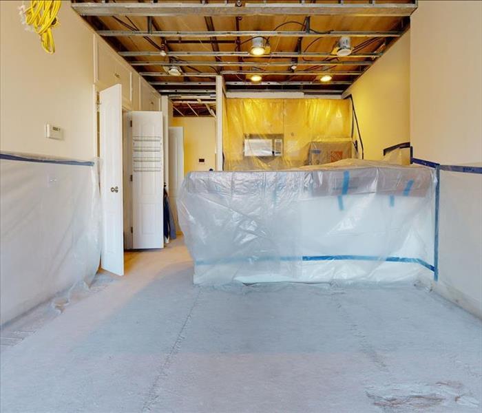 An apartment with a kitchenette sealed with polyethylene sheeting, taped walls, removed flooring, and removed ceiling sheetro