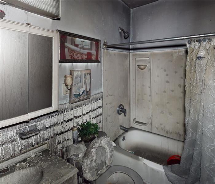 A heavily fire-damaged bathroom with charred tile, counters, mirrors, sink, and toilet, among other belongings