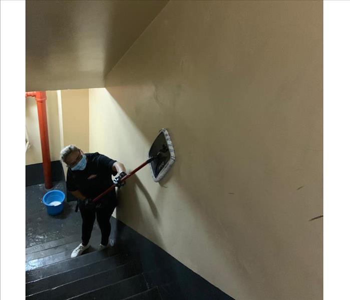 SERVPRO tech wiping down stairwell walls and ceiling from soot