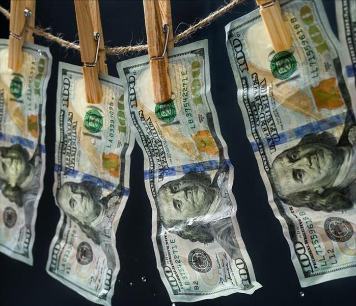 Hundred dollar bills hanging on a clothes dryer line. 